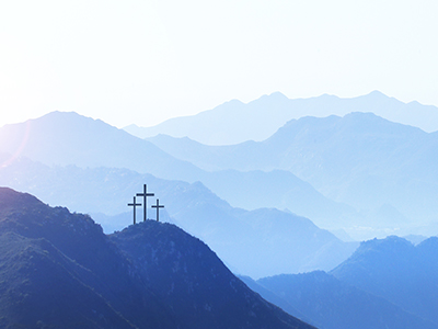 Three crosses on a hill at sunrise symbolize the Crucifixion of Christ  as the sun rises in the distance.  A series of mountain ridges disappear into the horizon